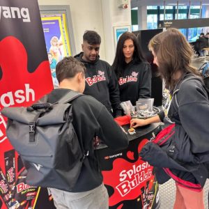 Deux étudiants goûtent la sauce Buldak à un stand derrière lequel se tiennent deux ambassadeurs de la marque Buldak