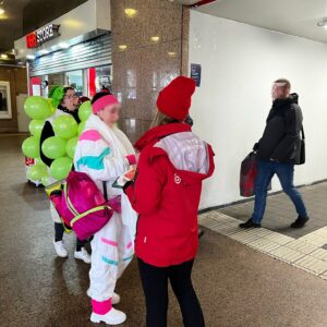 Une promotrice de la Rheinbahn remet un dépliant à deux filles déguisées
